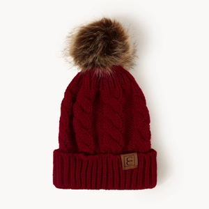Close-up of deep red cable knit beanie featuring a brown fur pom-pom and leather logo patch