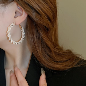 Détail du mannequin portant des boucles d'oreilles dorées enveloppées de perles blanches