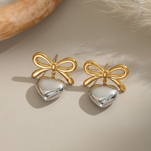 Detail shot of two-tone bow earrings with silver heart pendants on a rustic background