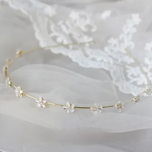 Dettaglio di un cerchietto dorato con delicati fiori bianchi e strass brillanti incastonati
