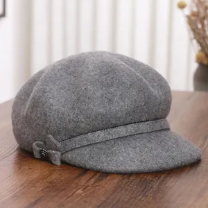 Elegant grey wool newsboy cap with bow decoration on a rustic wooden table surface