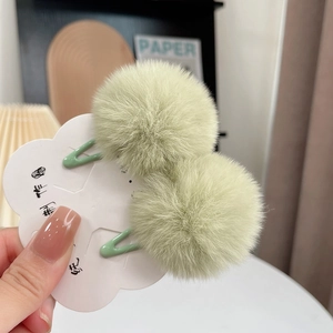Pair of green faux fur pom pom hair clips for kids on decorative card holder