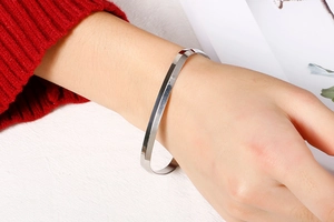 Macro shot of silver geometric faceted open cuff bracelet worn with a red knit sleeve