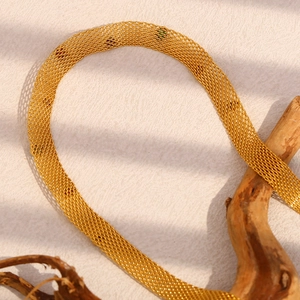 Close-up of a 18K gold-plated mesh chain necklace with colorful zircon on a textured surface