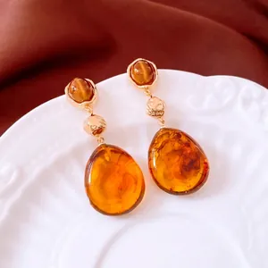 Vintage amber resin waterdrop earrings with gold trim on white ceramic and velvet