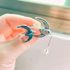 Dettaglio spilla a forma di rondine argento con smalto verde, strass e perla pendente