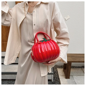 Detail of red pumpkin-shaped crossbody bag with gold chain strap on female model