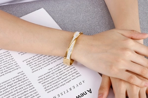 Detail of gold twisted pavé crystal bangle on a hand over a magazine background