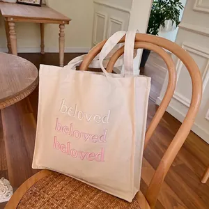 Cream canvas tote bag with pink gradient beloved embroidery on vintage chair