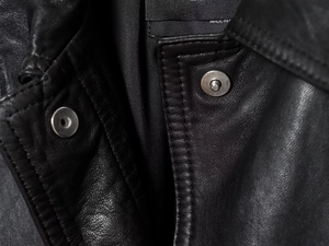 Gros plan sur la texture du cuir noir avec coutures détaillées et bouton-pression en métal