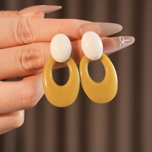 Close-up of retro oval hoop earrings in white and amber brown resin on model ear