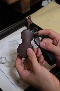 Detailed view of hand-held dark brown leather violin keychain with metal hardware and sheet music
