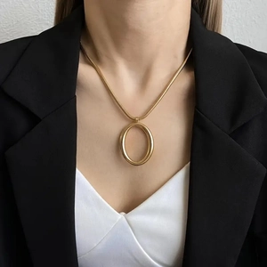 Detail of a minimalist 18k gold plated snake chain with a large oval pendant on a model