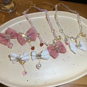 Elegant jewelry set with fabric bows, pearls and heart pendants on a ceramic tray