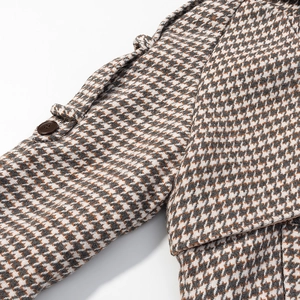 Macro view of houndstooth wool coat detail with decorative cuff strap and dark button