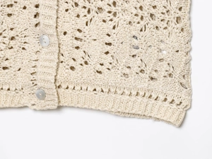 Close-up of beige crochet cardigan featuring hollow patterns and pearl buttons