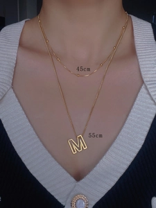 Close-up of layered 18k gold plated stainless steel necklaces with letter M pendant