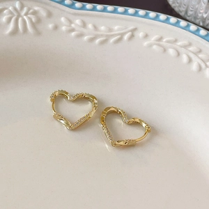 Close-up of gold heart hoop earrings with cubic zirconia on a white ceramic plate
