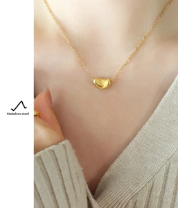 Macro detail of a golden bean pendant necklace in stainless steel worn by a model