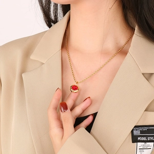 Detail of red round stone pendant with golden twist chain on model's beige suit jacket