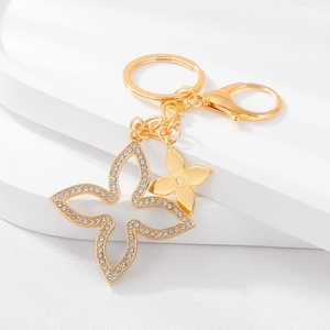 Sparkling diamond-set clover and butterfly keychain in golden finish on a white podium