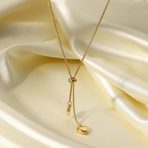 Dettaglio della collana dorata a Y con ciondolo a cuore su elegante seta color champagne