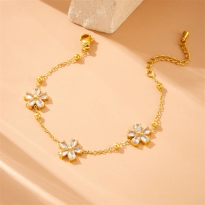 Elegant gold-plated bracelet with three cubic zirconia flower charms on a stone background
