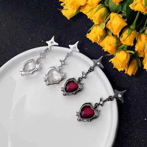 Silver star and dark red heart drop earrings with zircon crystals on a white ceramic plate