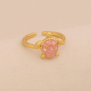 Detailed close-up of a golden turtle ring with a pink geometric shell on beige fabric