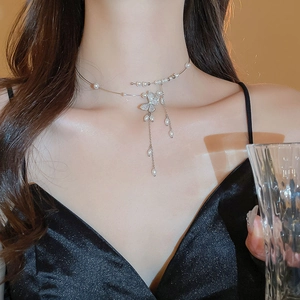 Detail of silver necklace with butterfly pendant, pearls, and long tassel chain on neck