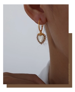 Detail of elegant gold-plated heart earring with white mother-of-pearl and small pearls