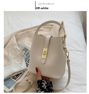 Detail of beige leather bucket bag with golden buckle on a white cloth and blazer