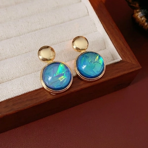 Elegant gold round resin earrings with iridescent teal stones on a vintage wood display