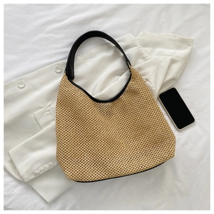 Flat lay of beige woven shoulder bag with black strap on white fabric with accessories