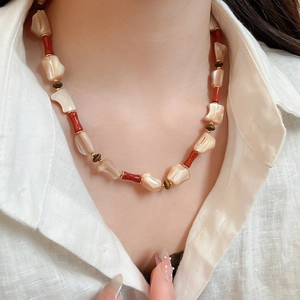 Detail of irregular shell beads necklace with red tubes worn on white shirt