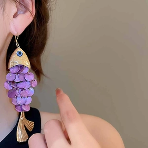 Detailed view of long purple fish-shaped earrings with gold metal and layered scales