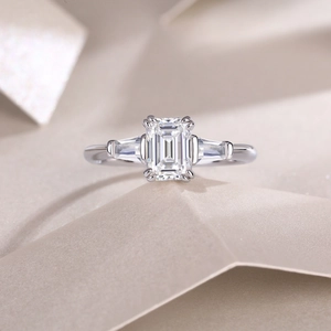 Macro shot of emerald cut moissanite ring with side stones on a textured background