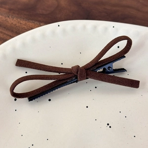 Macro view of dark brown suede bow hair clip on a minimalist ceramic plate