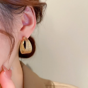 Close-up of golden textured C-shape hoop earrings with a layered luxury finish on model
