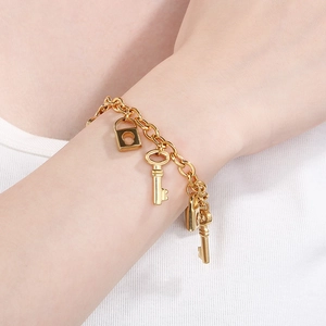 Detail view of a 18K gold plated stainless steel bracelet with key and lock charms on wrist