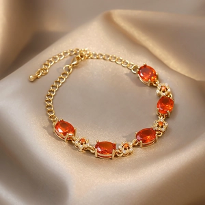 Détail du bracelet fleuri plaqué or aux pierres orange sur un tissu en soie satinée