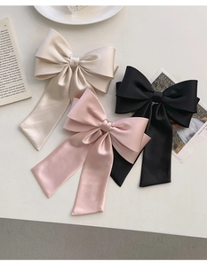 Detailed close-up of large satin bow hair clips in cream, pink and black on a desk