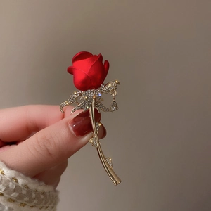 Detail of a 14k gold plated rose brooch with red petals and crystal teardrop pendant