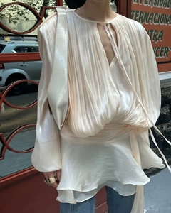 Detail showing cream pleated puff sleeve blouse with waist tie and ruffled hemline
