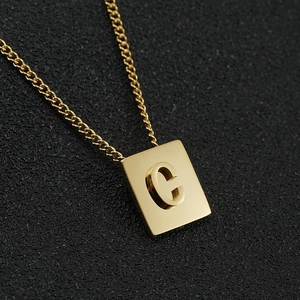 Detailed close-up of a gold square pendant with a 3D letter C on a black textured surface