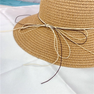 Detail of light brown woven straw sun hat with decorative cream and coffee bow