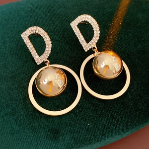 Detailed close-up of golden D-letter earrings with pavé crystals on green velvet