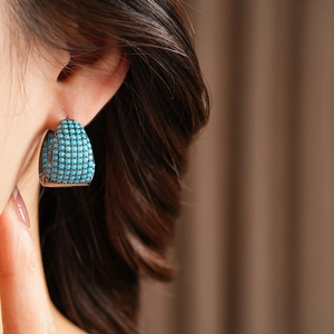 Detailed close-up of C-shape hoop earrings with turquoise stones on a female model
