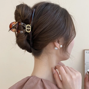 Détail d'une pince à cheveux écaille avec logo CD doré sur une coiffure élégante