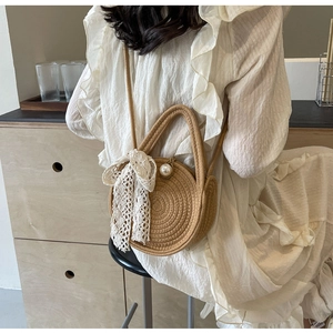 Detail of round straw bag with lace bow and large pearl clasp worn with a white dress